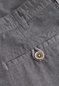 Shorts in tessuto grigio con finitura testurizzata, una tasca frontale e un anello intrecciato con un dettaglio in metallo.