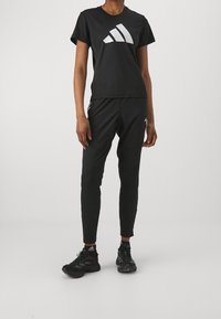 Czarna sportowa koszulka z białym logo adidas, zestawiona z czarnymi zwężanymi spodniami oraz czarnymi butami do biegania z zielonymi akcentami.