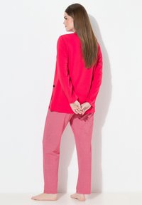 Maglietta rossa a maniche lunghe con spacchi laterali, abbinata a pantaloni pigiama rossi a fantasia con un motivo a diamante. Tessuto morbido, vestibilità casual.