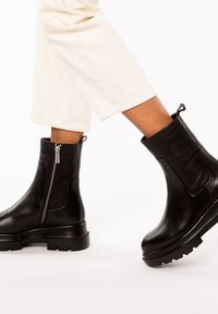 Svarta läderankelboots med en kraftig sula, sidodragkedja och en elegant design, kompletterad med en slät yta och robust konstruktion.