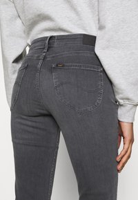 Jeans ajustados de denim en gris oscuro, con bolsillos traseros con costuras curvas y una etiqueta de cuero en la cintura.