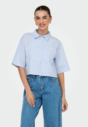 Camisa abotonada recortada en azul claro con rayas verticales blancas, mangas cortas y un bolsillo en el pecho, combinada con jeans azul claro.