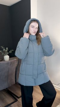 Light gray puffer jacket with a high collar, oversized fit, and a hood. Features button closure and visible quilted pattern.