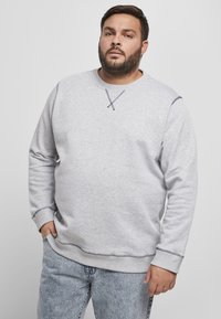Grå hettegenser med lange ermer og rund hals. Har kontrastsømmer og en avslappet passform. Kombinert med lyseblå denimjeans.