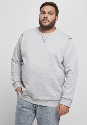 Sweatshirt gris à manches longues et col rond. Présente des coutures contrastantes et une coupe décontractée. Associé à un jean en denim bleu clair.