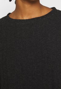 Czarny sweter dziany o prążkowanej fakturze, z szerokim dekoltem i delikatnym połyskiem. Materiał wydaje się miękki i lekko rozciągliwy.