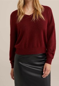 Burgundowy sweter dzianinowy z dekoltem w serek, długimi rękawami i prążkowanymi mankietami, w połączeniu z czarną ołówkową spódnicą z sztucznej skóry. Wyczuwalna miękka tekstura.