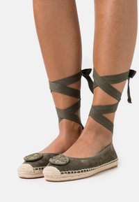 Ballerines en daim vert avec des accents décoratifs ronds, des rubans de cheville et une bordure en jute tressé. Texture lisse et design à bout fermé.