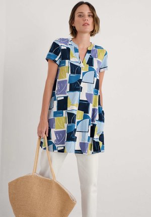 Kurzärmlige Tunika in einem bunten geometrischen Muster mit blauen, grünen und lila Formen; sie hat einen V-Ausschnitt und zwei Seitentaschen.