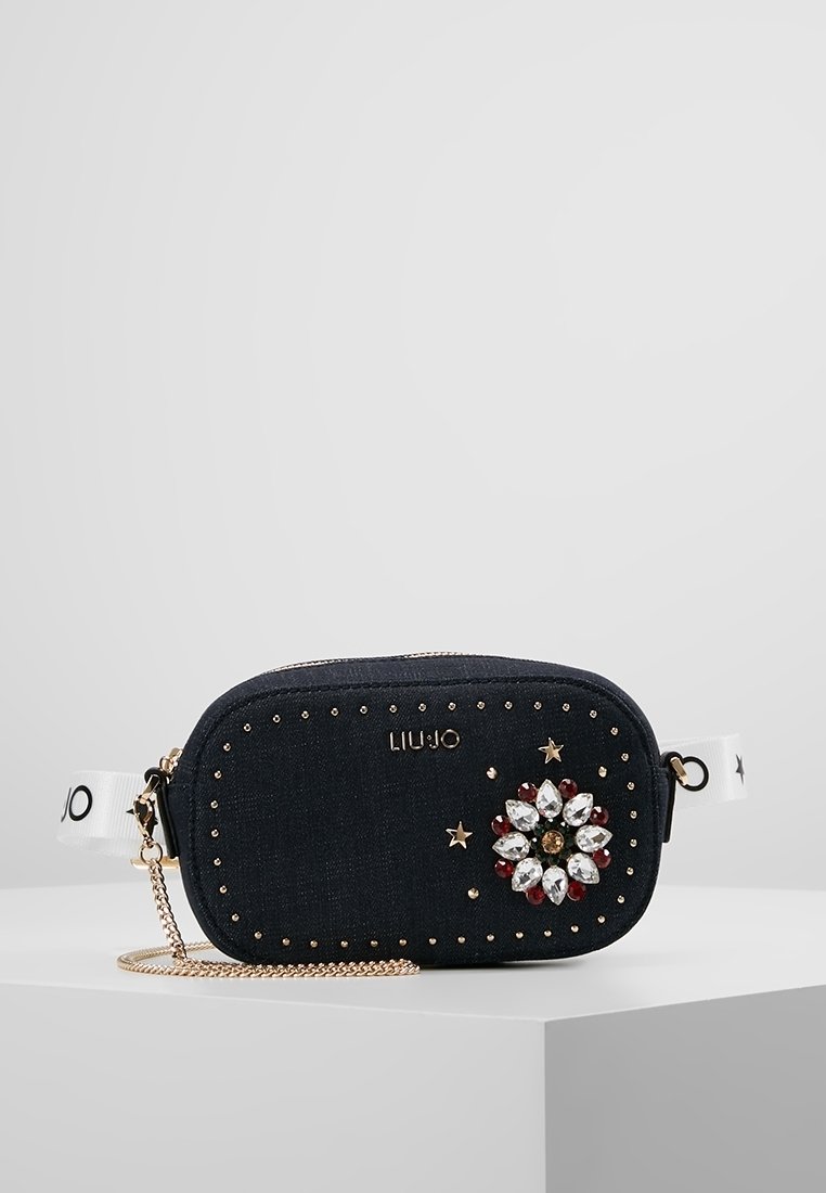 Borsa a tracolla in denim blu con borchie dorate, decorazione floreale in gemme e una tracolla a catena. Presenta una tracolla con logo bianco e una forma arrotondata.