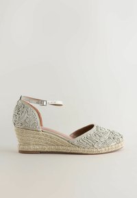 Espadrille compensée beige avec bride à la cheville et broderie tourbillonnante complexe sur les panneaux avant et arrière, semelle en corde texturée.