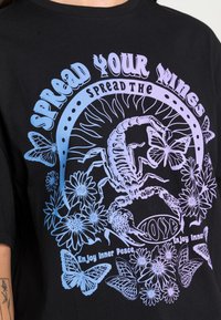 Camiseta de algodón negra con un gran gráfico multicolor que presenta un escorpión, mariposas y flores. El texto dice: "Despliega tus alas."
