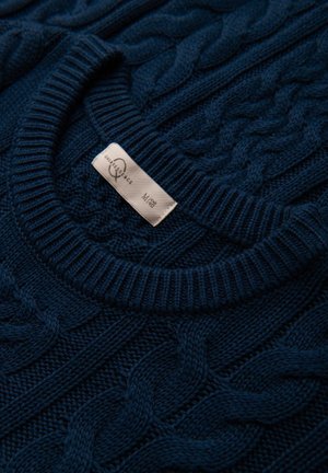 Marineblauwe gebreide trui met een kabelbreipatroon, geribbelde halslijn en manchetten, met een label waarop merk- en maatinformatie staat.