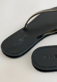Sorte flipflops med transparente stropper, tekstureret sort sål og præget "NEXT"-logo. Sømmede kanter og minimalistisk design.