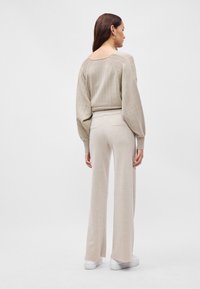 Μπεζ πλεκτό πουλόβερ με ριγωτή υφή και μανίκια μπαλονιού, συνδυασμένο με μπεζ παντελόνι με φαρδιά πόδια. Και τα δύο ρούχα διαθέτουν μαλακό, ελαφρύ ύφασμα.