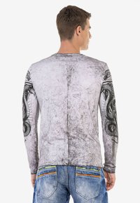Langärmliges Shirt in strukturiertem Grau mit schwarzen Schlangendesigns auf den Ärmeln. Verfügt über einen Rundhalsausschnitt und eine körperbetonte Silhouette.