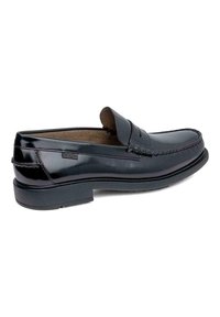 Mocasines de cuero negro con punta redondeada, costuras decorativas y una suela de goma texturizada y baja. El forro interior presenta un color marrón claro.
