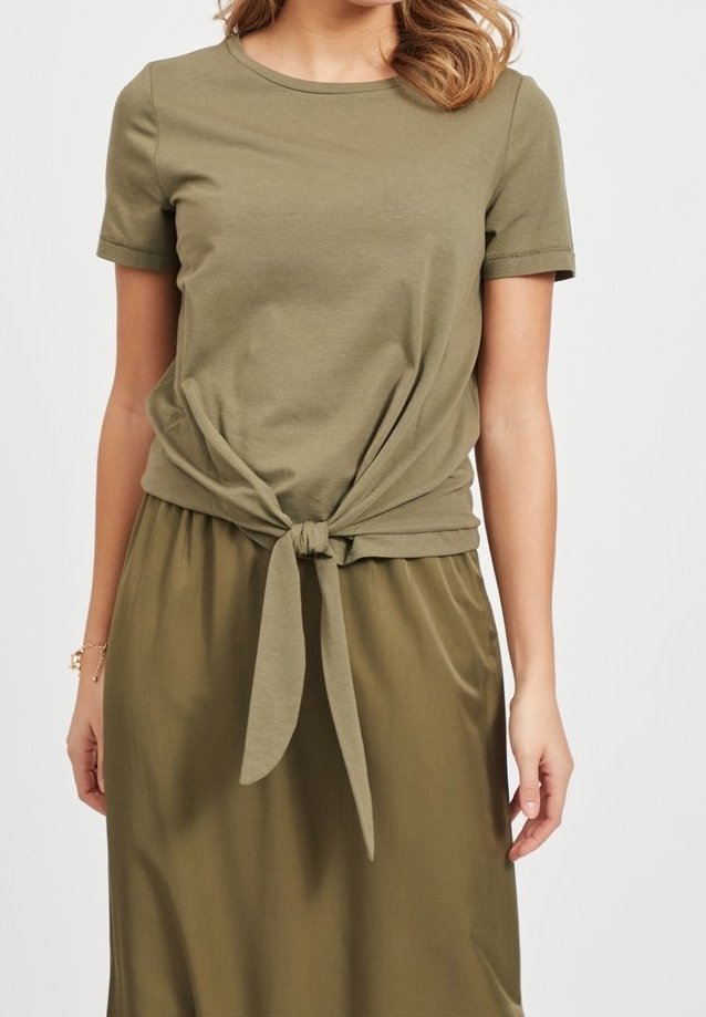 Femme portant un haut à manches courtes vert olive noué à l'avant, associé à une jupe assortie de couleur vert olive.