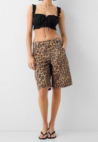 Černý zkrácený top s volánovými ramínky je spárován s leopardím vzorem, šortkami po kolena. Šortky mají boční kapsy a zapínání na knoflík.