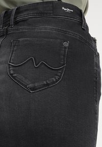 Černé džíny z denimu s výrazným designem zadní kapsy s zakřiveným šitím. Viditelný štítek na pase, zapínání na zip a knoflík.