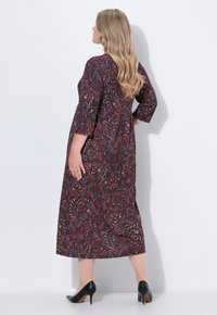 Pitkä musta mekko, jossa on värikäs paisley-kuvio, kolmivartiset hihat ja pitkänomainen siluetti. Yhdistetty mustiin korkeakorkoisiin kenkiin.