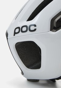 Casco de bicicleta blanco con acentos negros, que cuenta con aberturas de ventilación y una superficie texturizada negra en la parte inferior. Logo de la marca "POC" mostrado.