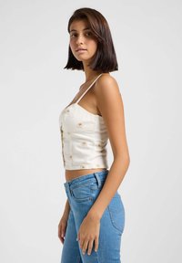 Hvit croppet topp med tynne stropper og blomsterdekorasjoner, parret med blå høyt liv bukser. Enkel og tettsittende design.