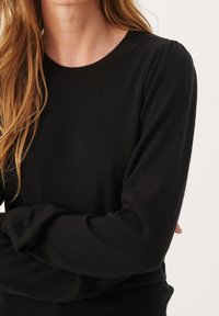 Sort strikket sweater med rund halsudskæring og lange ærmer, der har en afslappet pasform og blød tekstur. Subtil skulderdetaljering tilføjer dimension.