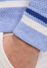 La manica di un maglione lavorato a maglia azzurro presenta un motivo a spina di pesce con strisce blu scuro e bianche. Texture morbida, polsino rifinito.