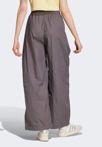 Wide-legged, lightweight gray pants with an elastic waistband, made of ripstop fabric. Paired with white sneakers for a casual look.