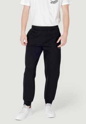 Pantaloni sportivi neri con vita elastica, caviglie a costina e tasche laterali. Completati da una maglietta bianca e sneaker bianche.