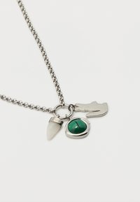 Κολιέ με αλυσίδα από ασήμι με τρεις γοητείες: λευκό αιχμηρό λίθο, πράσινο οβάλ πολύτιμο λίθο και ασημένιο φιγούρα κροκοδείλου σε λευκό φόντο.