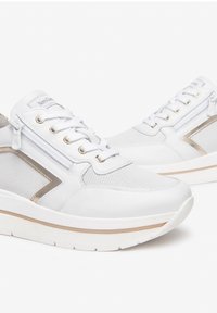 Baskets blanches avec une tige en mesh et cuir, des lacets plats, des accents dorés et une semelle rembourrée légèrement surélevée.