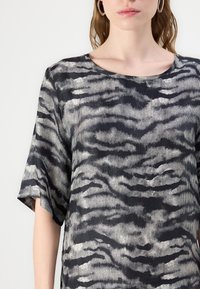 Schwarz- und grau gemusterte Bluse mit kurzen Ärmeln. Verfügt über einen weiten Ausschnitt und einen strukturierten Stoff, der ein wellenartiges Design über die Oberfläche schafft.