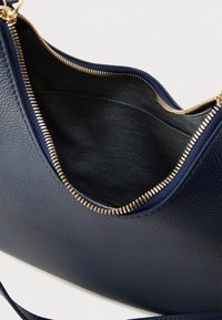 Tumši zils ādas rokassomiņa ar zelta rāvējslēdzēja detaļu, ar mīkstu tekstūru un plašu melna auduma iekšpusi.