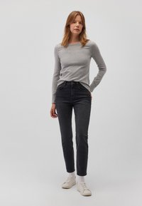 Graues langärmliges Oberteil, tailliert. Schwarze High-Waist-Jeans, Slim Fit. Weiße Sneakers mit strukturierter Oberfläche und hellen Sohlen. Einfache Hintergrund.