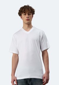 T-shirt bianco a scollo a V, maniche corte, realizzato in tessuto leggero. Presenta una vestibilità comoda e una texture liscia. Abbinato a jeans blu.