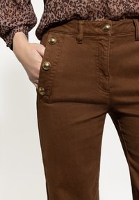 Brown pants with a smooth texture, featuring gold button accents on the left pocket and a classic five-pocket design.