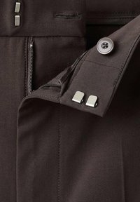 Bruine stof met een rits- en knoopsluiting. Heeft metallic accenten en een gladde textuur. Bevat stikdetails op de stof.
