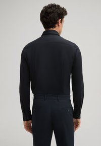 Herren schwarzes Langarmhemd mit glatter Textur, mit umgeschlagenem Kragen und knöpfbaren Manschetten. Schmal geschnitten, kombiniert mit dunklen Hosen.