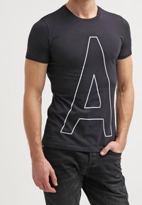 Mustat lyhyet hiharat t-paita, jossa on iso valkoinen "A" -grafiikka painettuna etuosaan, valmistettu kevyestä, sileästä kankaasta.