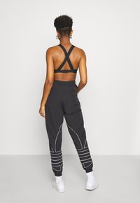 Sujetador deportivo negro con diseño de espalda cruzada, combinado con pantalones de chándal negros con costuras de acento en blanco y puños elásticos.