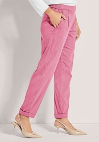 Roze chino's met een ontspannen pasvorm, voorzien van zijzakken en opgerolde manchetten. Gecombineerd met beige slingback hakken, die een gladde textuur benadrukken.