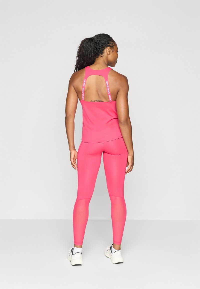 Débardeur de sport rose ajusté avec un dos décolleté, associé à un legging rose assorti. Les deux sont fabriqués dans un tissu lisse et extensible.