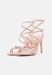 Sandales à talons hauts rose clair avec des embellissements floraux, un design à lanières et une finition brillante. Comprend des brides ajustables à la cheville et un bout pointu.