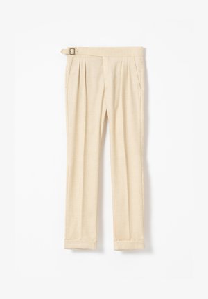 Pantalones beige a medida con pinzas delanteras, bolsillos laterales, dobladillos con vuelta y hebilla lateral ajustable en la cintura.
