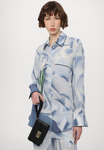 Silk blouse with a blue and white abstract pattern, featuring a chest pocket, button closures, and contrasting black piping details.