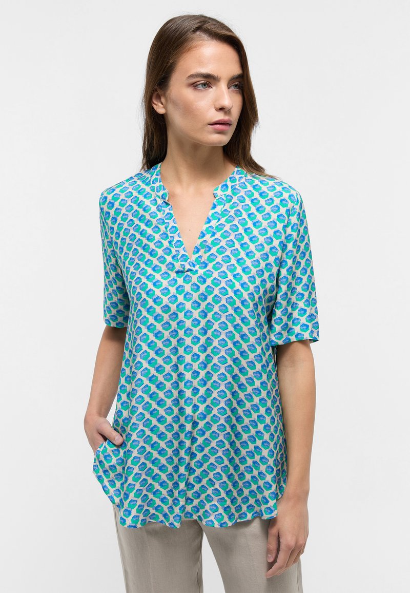 Short-sleeve blouse in light blue with a geometric pattern in green and dark blue. V-neckline and relaxed fit, made of lightweight fabric.