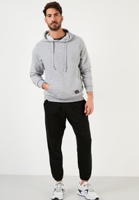 Gray hoodie with a kangaroo pocket, drawstring hood, and ribbed cuffs. Paired with black tapered joggers and white sneakers.