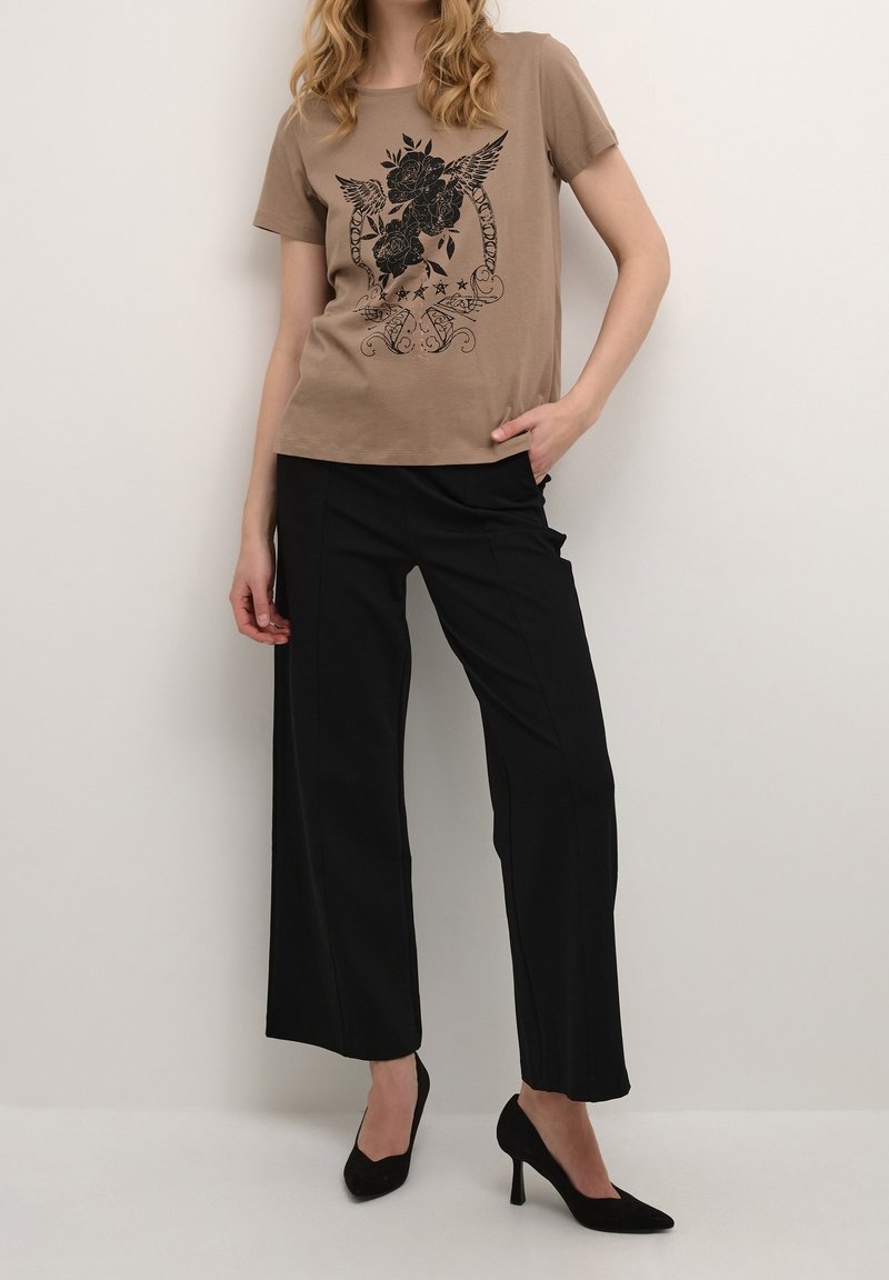 T-shirt beige avec impression florale noire et col rond, associé à un pantalon noir à jambes larges et des talons hauts noirs.